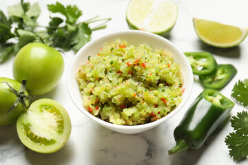 Tasty salsa in bowl and ingredients on white marble table, closeup