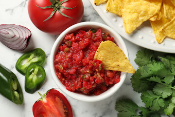 Tasty salsa in bowl, ingredients and nachos on white marble table, flat lay