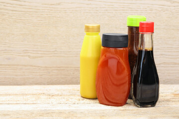 Different tasty sauces in bottles on wooden table. Space for text