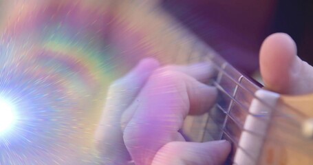 Pressing musician's left hand forming chord on acoustic guitar strings in studio with rainbow flare
