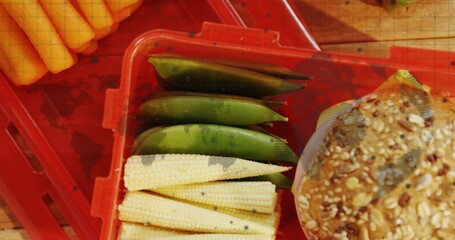 Resting red crate containing baby corn, sugar snap peas and seeded grain bun on kitchen countertop