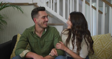 Sitting couple wearing casual wear on sofa at home, with yellow cushion and plant by staircase