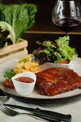 Grilled ribs and side dishes presented on a plate, alongside a glass of wine