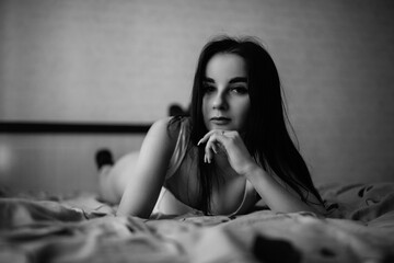 Woman with long dark hair, lying on bed in soft light, showcasing relaxed pose and intimate atmosphere, emphasizing comfort and tranquility in a cozy bedroom setting
