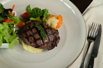 Delicious grilled steak served with various vegetables on a white plate, ready to be enjoyed. The presentation of the meal is neat, with a focus on fresh ingredients.
