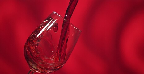 Red wine being poured into a glass with vibrant red background, elegant drink and celebration concept