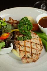 Deliciously grilled pork chop on a plate, served with a side of vegetables and sauce