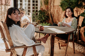 Women enjoying a friendly coffee conversation in an outdoor setting surrounded by greenery and warm...