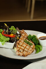 A Deliciously Grilled Pork Chop Dinner with Salad, Sauce, and Vegetables on a Plate