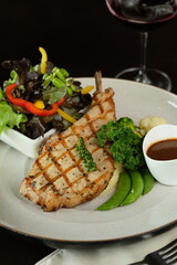 A delicious grilled pork chop served with a fresh salad and wine glass, a culinary delight. Featuring meticulously arranged grilled pork chop, complementing greens, and wine glass