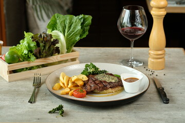 A gourmet steak dinner, complete with a glass of red wine, is beautifully arranged on a table