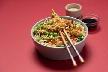 Asian noodle bowl with edamame beans, mushrooms and vegetables on dark red background, minimalist top view of healthy vegan meal