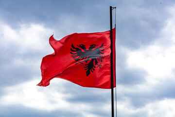Albanian flag with the black double-headed eagle emblem waving against a cloudy sky.