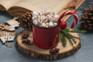 Close up of mug of hot cocoa with marshmallows and candy cane on wooden tree slice. Cozy Christmas winter drink concept