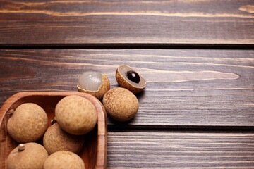 Longan tropical fruit displayed in a wooden bowl on a rustic wooden surface, showcasing its round shape and textured skin, emphasizing freshness and natural beauty