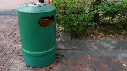 Obraz premium Green trash bin with built-in ashtray for smokers to dispose of ash or cigarette waste, placed outdoors in a public area for cleanliness and waste management.