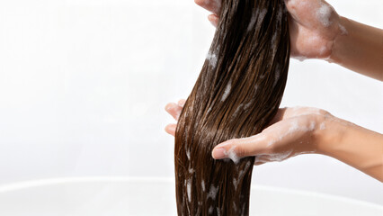 Woman’s hands gently washing long wet hair with foam, concept for shampoo, beauty routine, skincare and wellness banner

