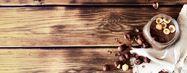 Natural hazelnut butter without sugar in glass jar on rustic wooden table — top view