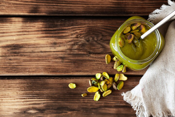 Natural pistachio butter without sugar in glass jar on rustic wooden table — top view