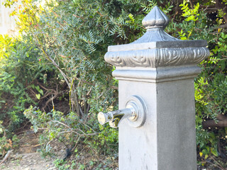 Fototapeta premium Ornate garden water fountain with metal spout in lush greenery