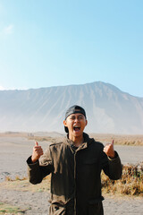 Excited Young Asian Traveler Celebrating at Mount Bromo Volcano Landscape, Indonesia. symbolizing freedom, adventure, and happiness.