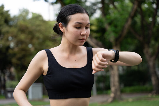 Young woman checking time on smartwatch while exercising outdoors. Concept of fitness tracking, workout routine, health monitoring, and active lifestyle with wearable technology.
