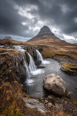 Majestic peak looms over cascading waterfalls in dramatic landscape under stormy sky