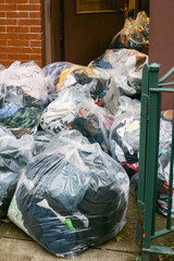 Bags of donated clothes piled outside door near brick wall in urban area