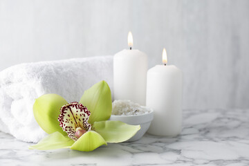 Beautiful spa composition with sea salt and burning candles on white marble table, closeup. Space...