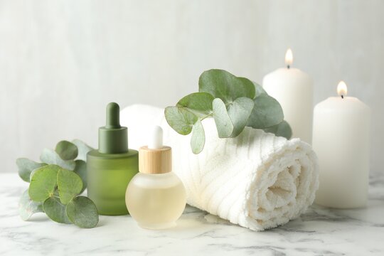Beautiful spa composition with essential oils and burning candles on white marble table, closeup - Powered by Adobe