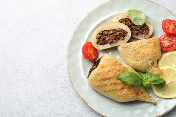 Pieces of tasty grilled squid stuffed with mushrooms, basil, tomatoes and lemon on light grey textured table, top view. Space for text