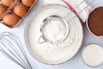 Ingredients for dough, whisk and strainer on white tiled table, flat lay