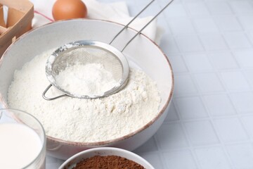 Ingredients for dough and strainer on white tiled table, closeup. Space for text
