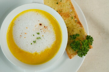 Delicious creamy soup with a side of garlic bread on a white plate. A close-up captures the appetizing meal with garnish
