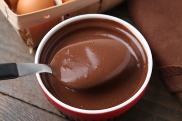 Taking liquid chocolate dough from bowl with spoon on wooden table, closeup