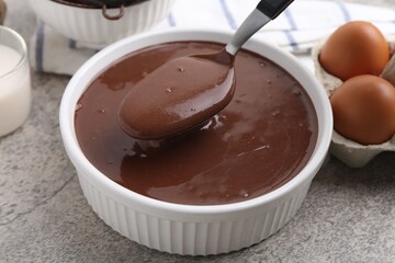 Taking liquid chocolate dough from bowl with spoon on grey table, closeup