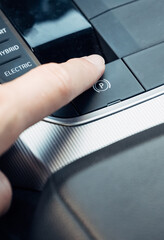Finger pointing at electronic parking brake in car with “P” symbol, close-up of vehicle control