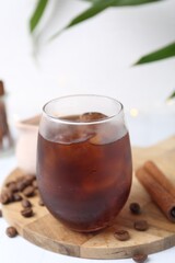 Tasty iced coffee in glass and beans on white table, closeup