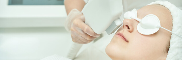 Young caucasian female receiving laser facial treatment at spa for skin rejuvenation.