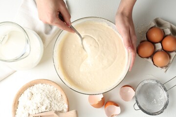 Woman making batter (liquid dough) at white table, top view