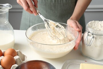 Woman making batter (liquid dough) at white table indoors, closeup