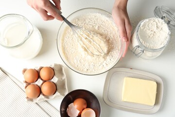 Woman making batter (liquid dough) at white table, top view