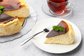 Piece of delicious Basque cheesecake with mint and tea on light grey table, closeup