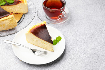 Piece of delicious Basque cheesecake with mint and tea on light grey table, closeup. Space for text