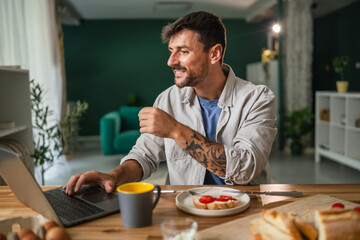 Man enjoying healthy breakfast while working on laptop at home