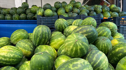 A vibrant street market scene with stacked watermelons in blue containers. 