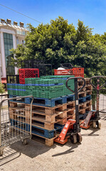 A cart for groceries is parked next to stacked pallets. The scene includes mesh containers