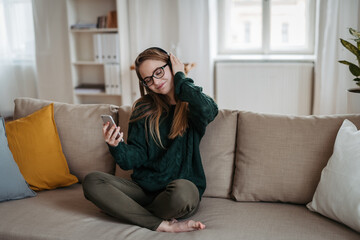 Obraz premium Teen girl relaxing on the couch and listening to music with headphones.