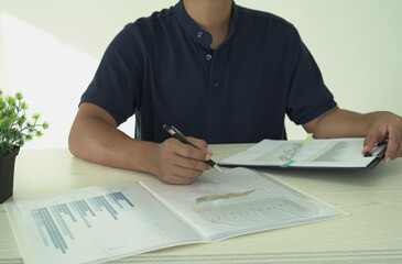 A real estate male agent is reading and checking paper documents, signing the lease agreement, preparing contract and terms and conditions details and checking data analysis as a remote freelancer.	