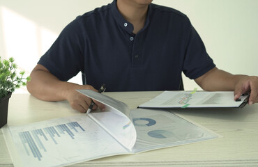 A real estate male agent is reading and checking paper documents, signing the lease agreement, preparing contract and terms and conditions details and checking data analysis as a remote freelancer.	